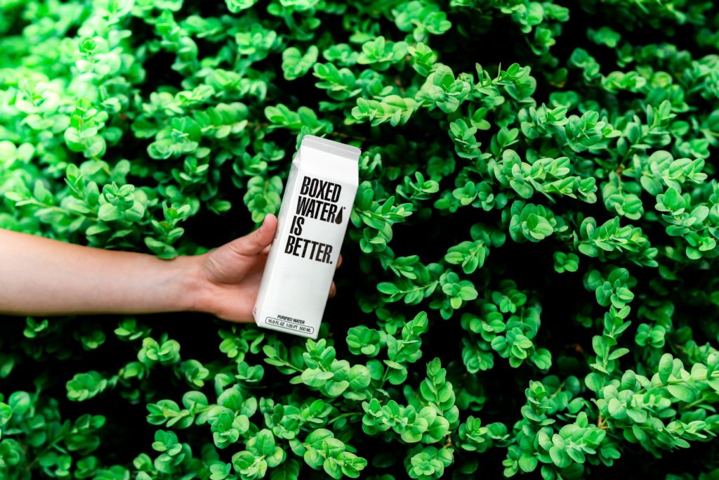white recyclable box with the words Boxed Water Is Better written on a green plant background