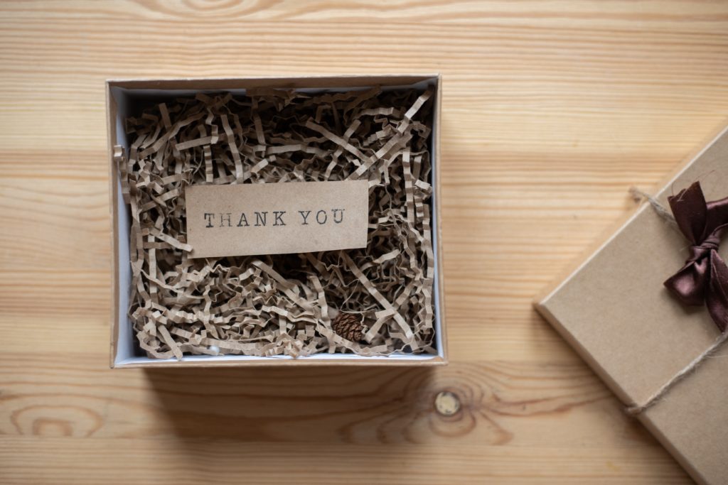 Cardboard box filled with strips of recycled material and a cardboard sign that says thank you.